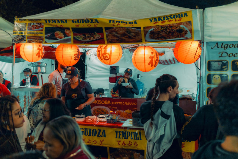 Bustling Asian street food market stall with illuminated lanterns and diverse crowd.