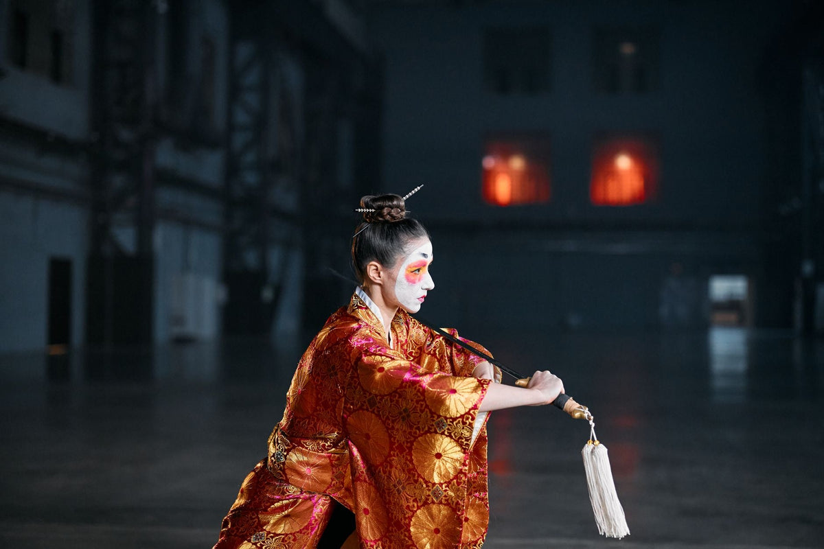 Woman in a traditional Japanese costume with makeup, performing indoors.