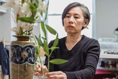 A focused florist carefully arranging flowers in a decorative vase inside a cozy room.